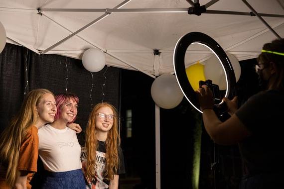 Three students posing for a photo in front of ring light with balloons in the background